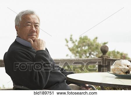 Stock Image - Senior Asian man sitting outdoors. Fotosearch
