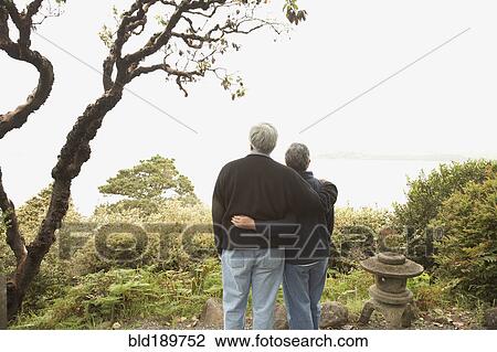 Stock Image - Senior couple standing arm in arm outdoors. Fotosearch