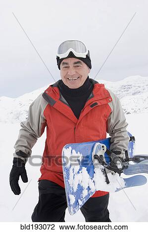 Stock Image - Senior Hispanic man snowboarding. Fotosearch