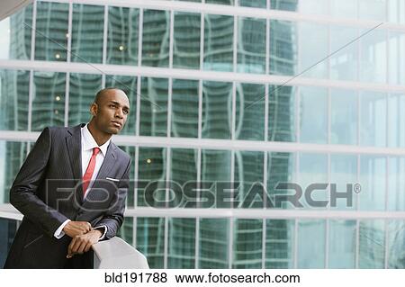 Stock Photo - Serious African businessman leaning on railing of urban balcony. Fotosearch