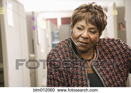Stock Image - Serious Black businesswoman standing in office talking on headset. Fotosearch