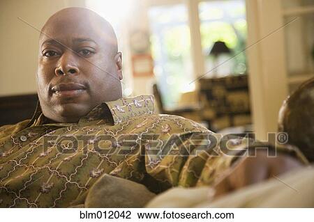Stock Image - Serious Black man sitting on sofa. Fotosearch