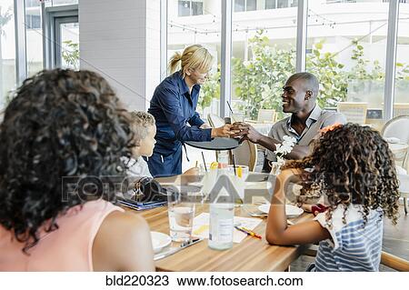Stock Image - Server bringing drinks for family at restaurant. Fotosearch
