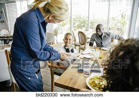 Stock Image - Server bringing food for family in restaurant. Fotosearch