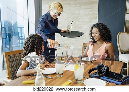 Stock Image - Server pouring water for mother and daughter at restaurant. Fotosearch