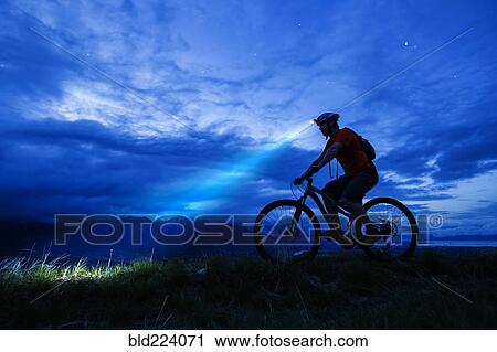 Stock Image - Silhouette of Caucasian man riding mountain bike at night. Fotosearch