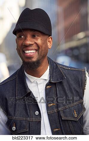 Stock Photo - Smiling African American man wearing hat and denim vest. Fotosearch