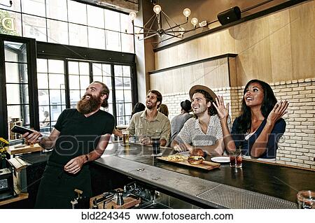 Smiling bartender and customers watching television in bar View Large Photo Image Stock Photography - Smiling bartender and customers watching television in bar. Fotosearch