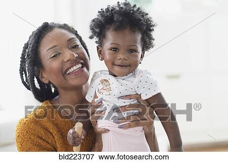Stock Photo - Smiling Black mother holding baby daughter. Fotosearch