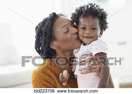 Smiling Black mother kissing baby daughter on cheek View Large Photo Image Stock Photo - Smiling Black mother kissing baby daughter on cheek. Fotosearch