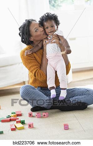 Stock Photograph - Smiling Black mother kissing baby daughter. Fotosearch
