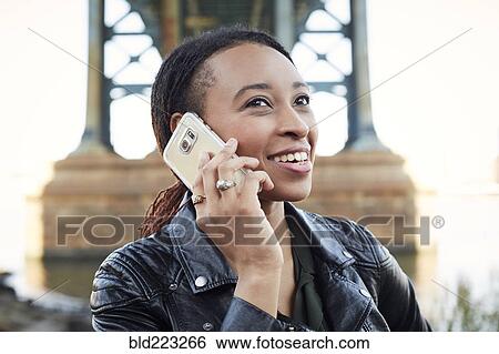 Smiling Black woman using cell phone at bridge View Large Photo Image Stock Photograph - Smiling Black woman using cell phone at bridge. Fotosearch
