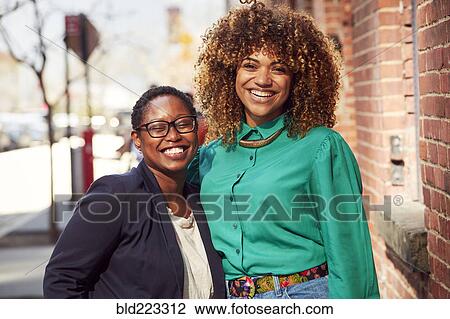 Stock Image - Smiling Black women posing on city sidewalk. Fotosearch