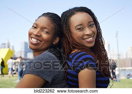 Stock Image - Smiling Black women sitting back to back. Fotosearch
