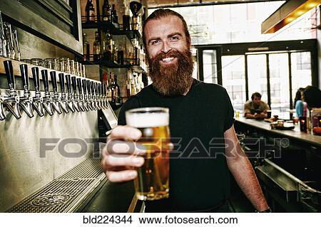Picture - Smiling Caucasian bartender serving beer at bar. Fotosearch