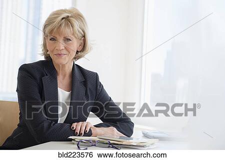 Smiling Caucasian businesswoman sitting at desk View Large Photo Image Stock Photograph - Smiling Caucasian businesswoman sitting at desk. Fotosearch