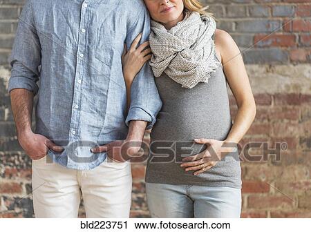 Stock Image - Smiling Caucasian expectant mother holding arm of man. Fotosearch