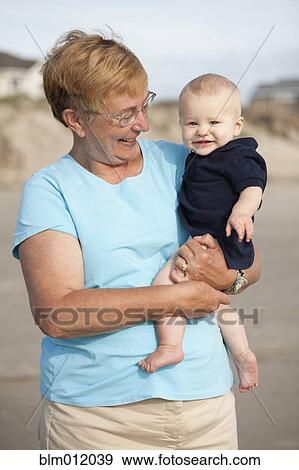 Stock Photo - Smiling Caucasian grandmother holding grandson on beach. Fotosearch