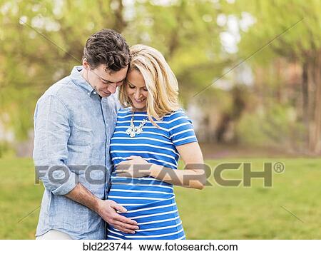 Smiling Caucasian man and expectant mother looking at belly View Large Photo Image Picture - Smiling Caucasian man and expectant mother looking at belly. Fotosearch