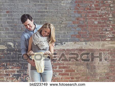 Smiling Caucasian man and expectant mother holding onesie View Large Photo Image Stock Photo - Smiling Caucasian man and expectant mother holding onesie. Fotosearch