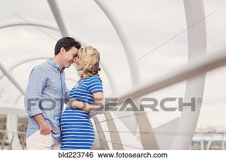 Stock Photograph - Smiling Caucasian man and expectant mother rubbing noses on walkway. Fotosearch
