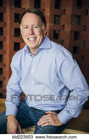 Stock Image - Smiling Caucasian man wearing jeans sitting. Fotosearch