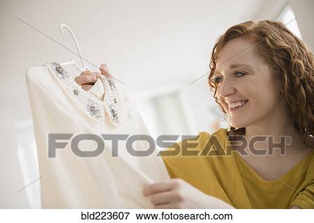 Stock Photo - Smiling Caucasian woman holding blouse on coathanger. Fotosearch