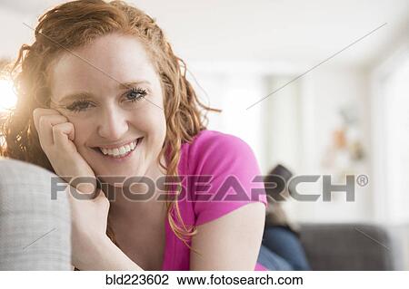 Stock Image - Smiling Caucasian woman laying on sofa. Fotosearch