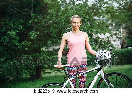 Stock Photo - Smiling Caucasian woman posing holding bicycle. Fotosearch