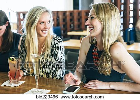 Stock Photograph - Smiling Caucasian women at bar with cocktails. Fotosearch