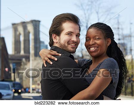 Stock Image - Smiling couple hugging in city. Fotosearch