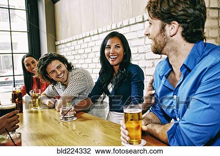 Stock Image - Smiling friends drinking at table in bar. Fotosearch