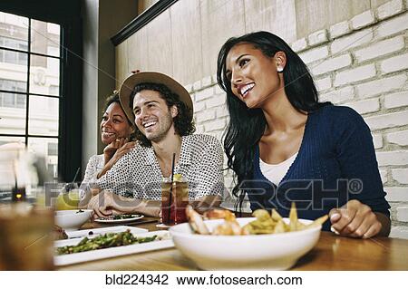 Smiling friends enjoying food and cocktails at table in bar View Large Photo Image Stock Image - Smiling friends enjoying food and cocktails at table in bar. Fotosearch