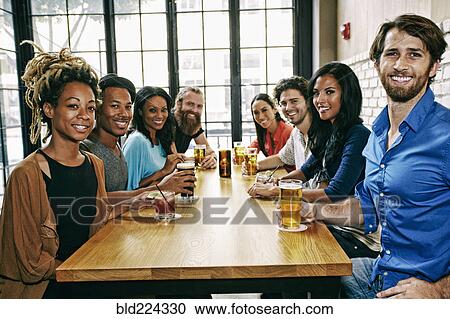 Stock Image - Smiling friends posing at table in bar. Fotosearch