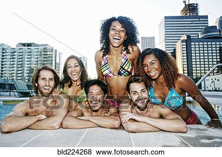 Smiling friends relaxing poolside at urban swimming pool View Large Photo Image Stock Photo - Smiling friends relaxing poolside at urban swimming pool. Fotosearch