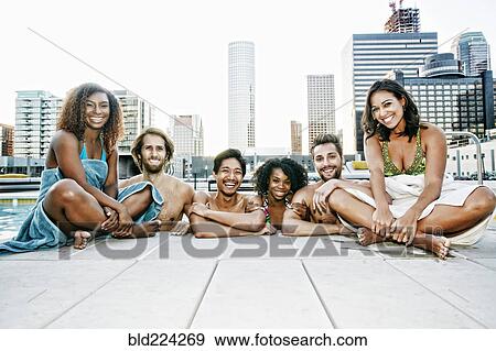 Stock Photo - Smiling friends relaxing poolside at urban swimming pool. Fotosearch