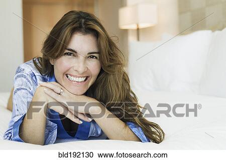Stock Image - Smiling Hispanic woman laying on bed. Fotosearch