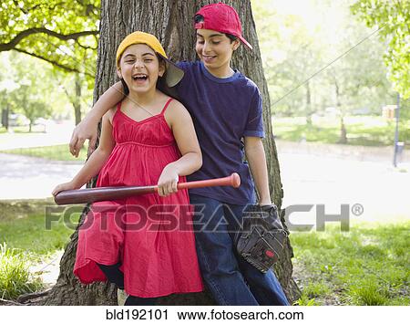 Stock Image - Smiling mixed race brother and sister holding baseball bat and mitt. Fotosearch