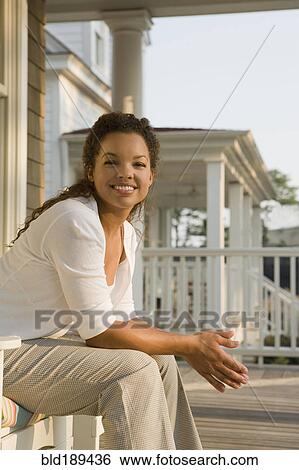 Stock Photograph - Smiling mixed race woman sitting on porch. Fotosearch