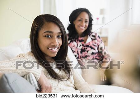 Stock Image - Smiling mother and daughter sitting on sofa. Fotosearch
