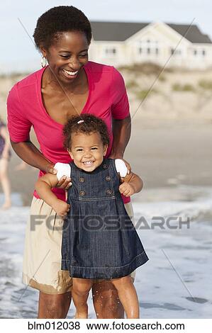 Stock Photo - Smiling mother playing with daughter on beach. Fotosearch