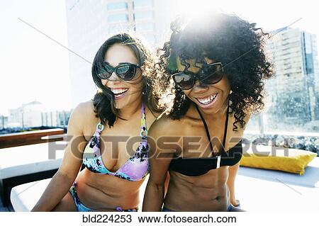 Stock Image - Smiling women wearing bikinis at urban poolside. Fotosearch