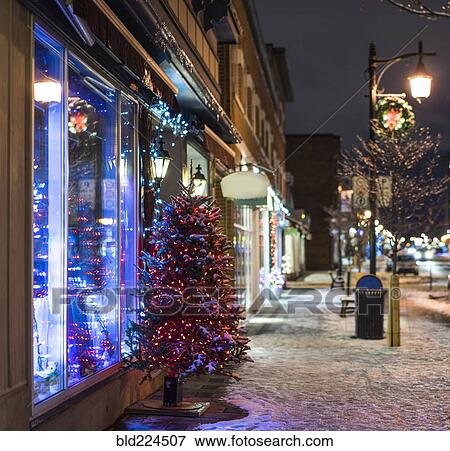 Stock Photo - Snow and Christmas tree on city sidewalk at night. Fotosearch