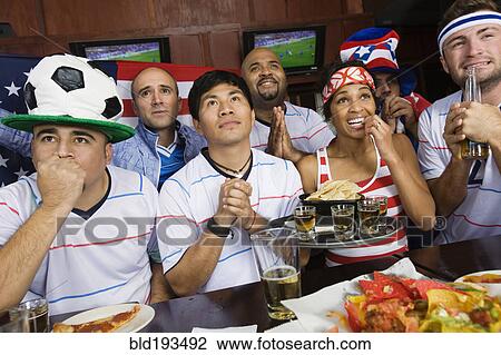 Stock Image - Sports fans drinking and eating in sports bar. Fotosearch