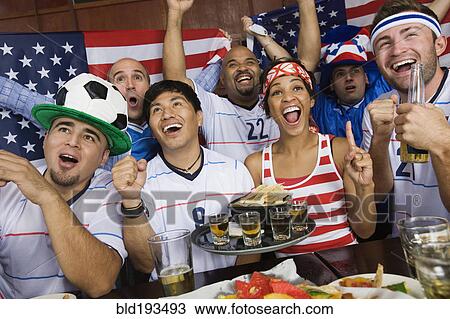 Stock Image - Sports fans drinking and eating in sports bar. Fotosearch