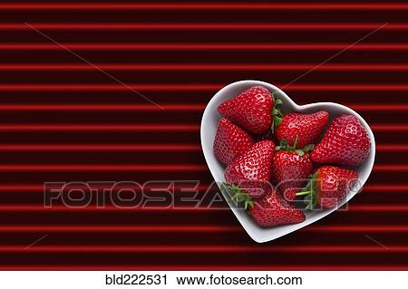 Stock Image - Strawberries in heart-shape bowl on red striped background. Fotosearch