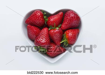 Stock Image - Strawberries in heart-shape bowl on white background. Fotosearch