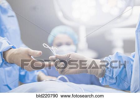 Stock Image - Surgeons handing forceps in operating room. Fotosearch