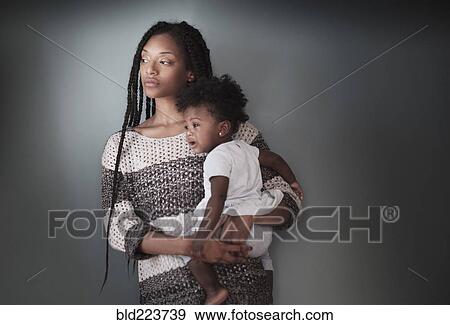 Thoughtful Black woman standing holding baby daughter View Large Photo Image Stock Photo - Thoughtful Black woman standing holding baby daughter. Fotosearch