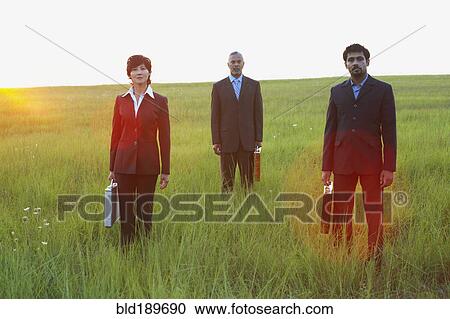Stock Image - Three businesspeople standing in field. Fotosearch